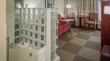A bathroom with a glass block partition, a bathtub, a red chair, a small table, and a patterned curtain.