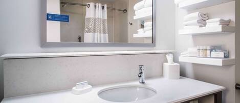 A bathroom with a large mirror, a sink, and shelves with towels.