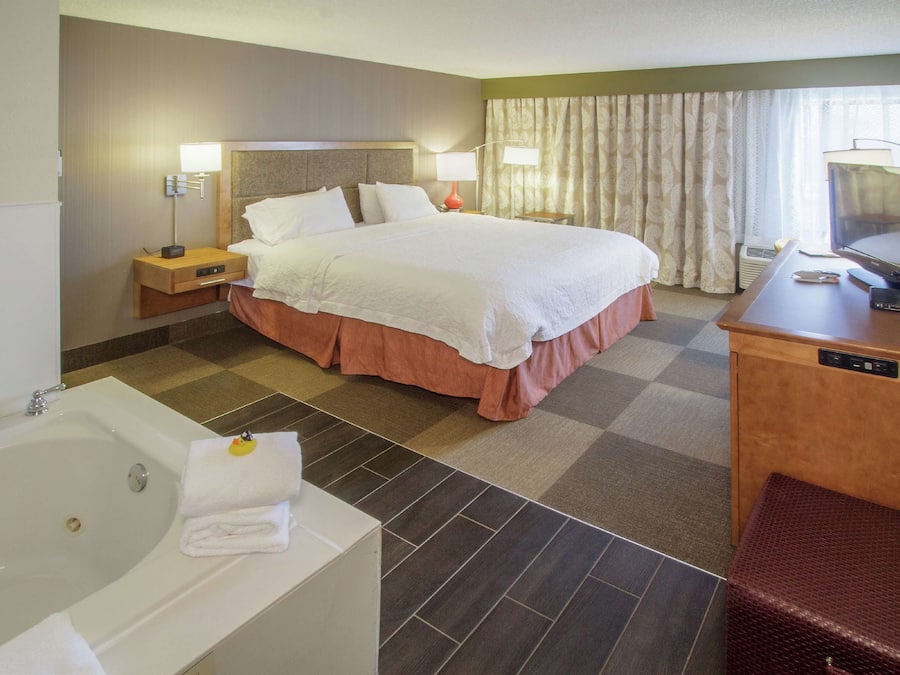 A hotel room with a large bed, a separate bathroom with a bathtub, a desk with a computer, and a television.