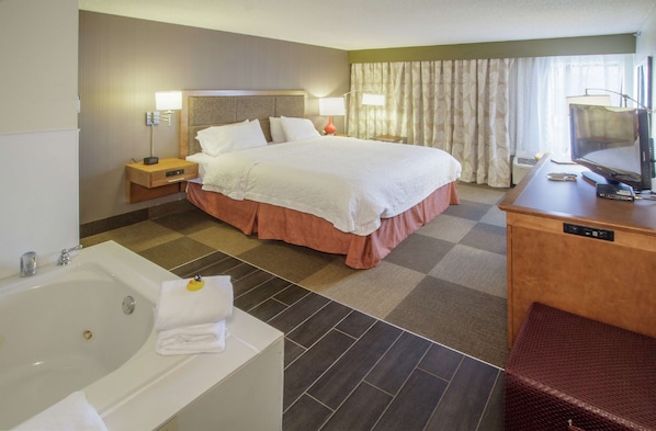 A hotel room with a large bed, a separate bathroom with a bathtub, a desk with a computer, and a television.
