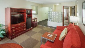 Una sala compacta con televisor, un refrigerador pequeño, un sofá rojo y una mesa de centro de madera.
