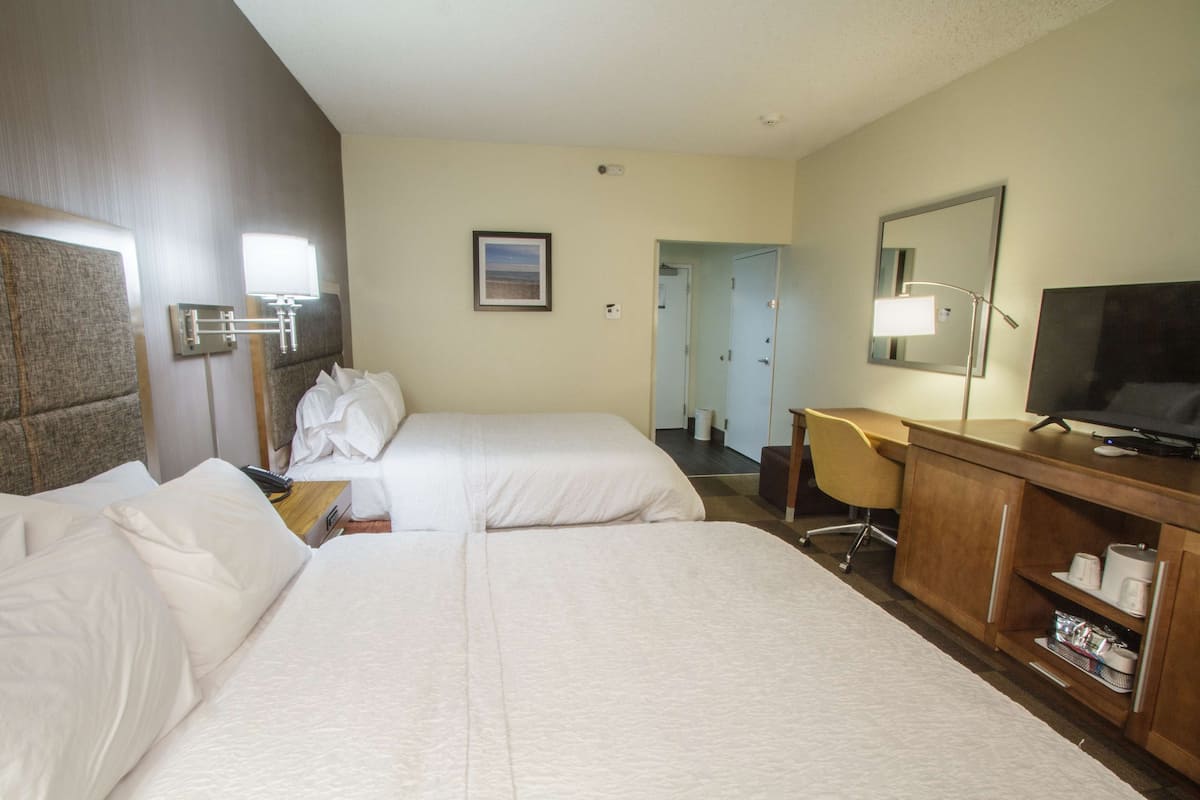 A hotel room with two beds, a desk, a television, and a bathroom visible through an open door.