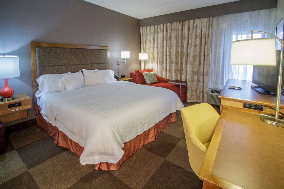 A hotel room with a large bed, a desk, a chair, a TV, and two lamps.