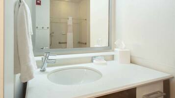 Une salle de bain avec un lavabo blanc, un miroir, une serviette suspendue à un porte-serviettes et un support à papier toilette.