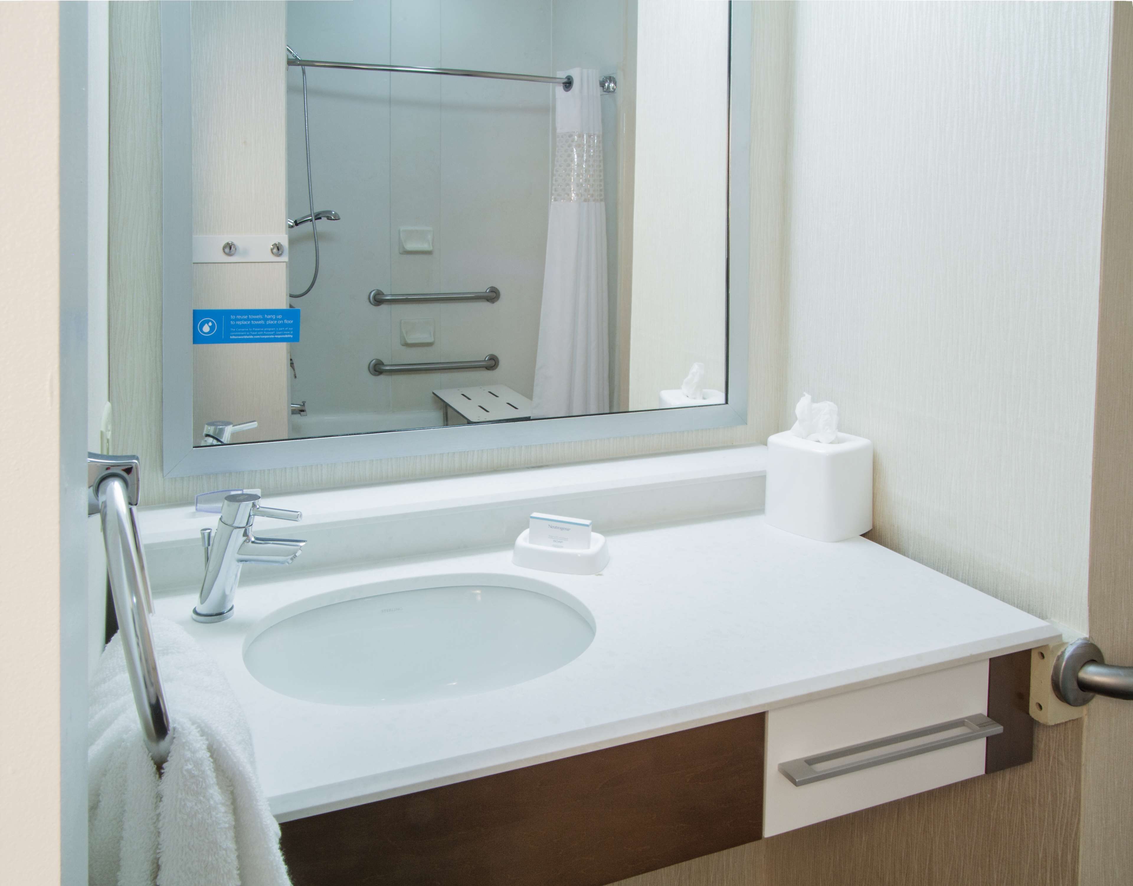 Un baño con lavamanos, espejo, toallero y secador de manos.