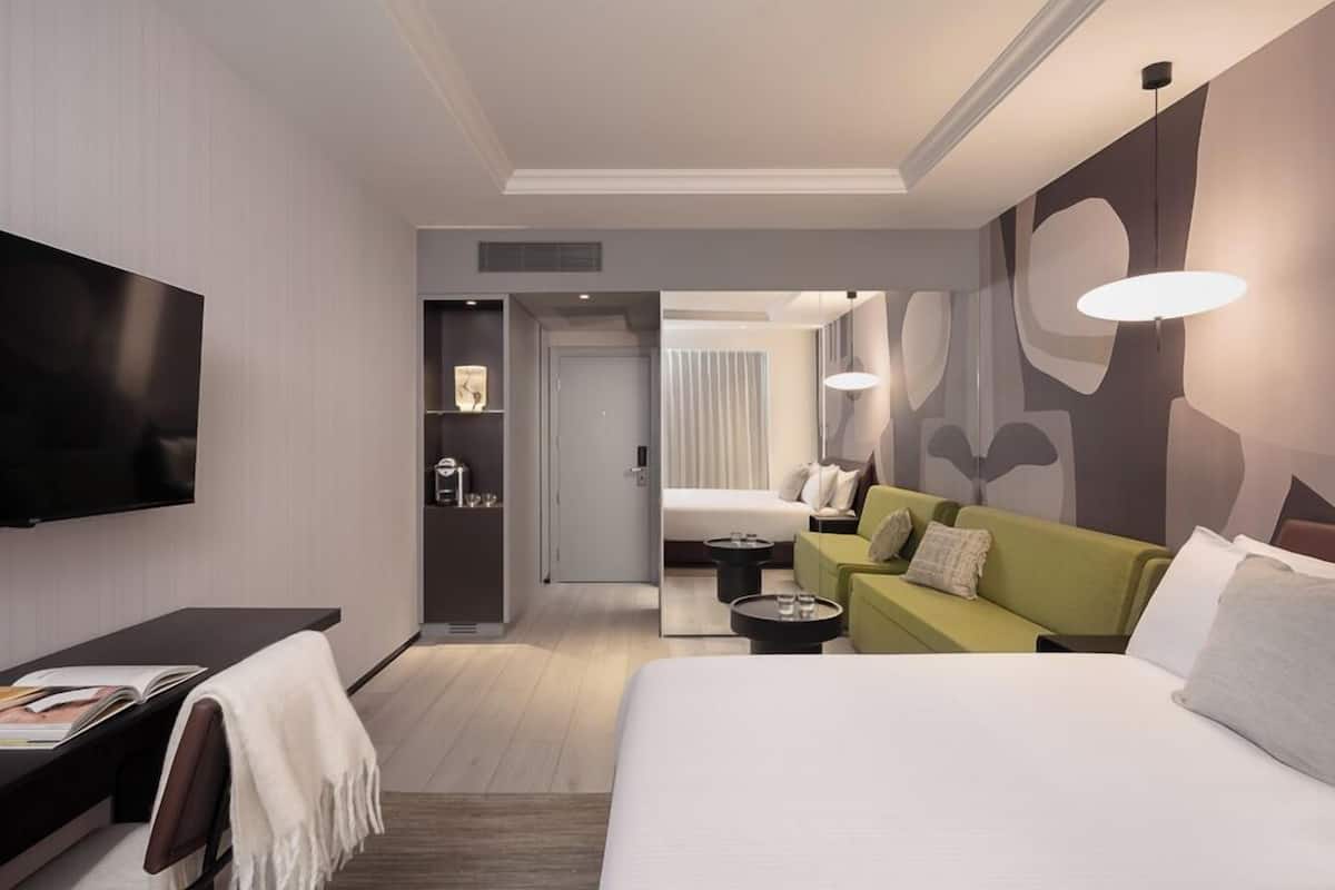 Une chambre d’hôtel moderne avec un grand lit, un canapé vert, un téléviseur à écran plat et une petite table.