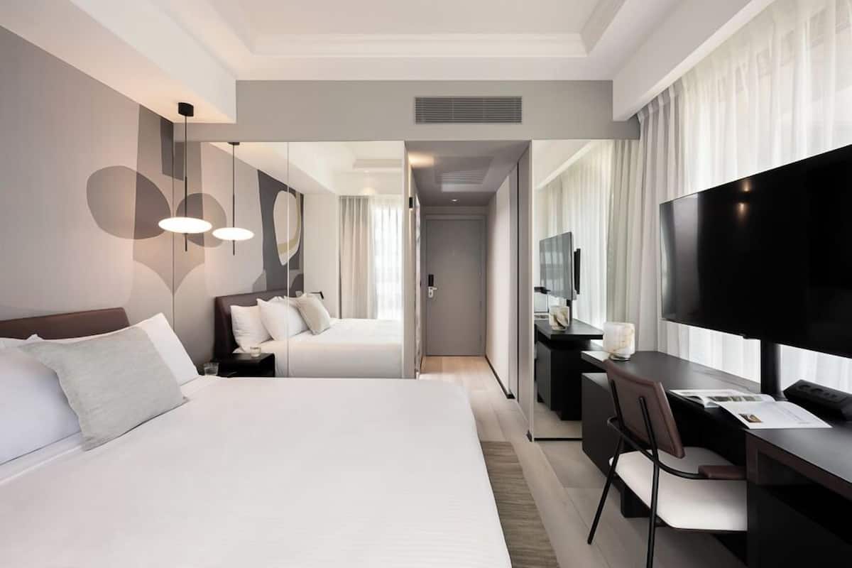 Une chambre d’hôtel moderne dotée d’un grand lit, d’un bureau avec une chaise, d’une télévision à écran plat et d’un miroir.