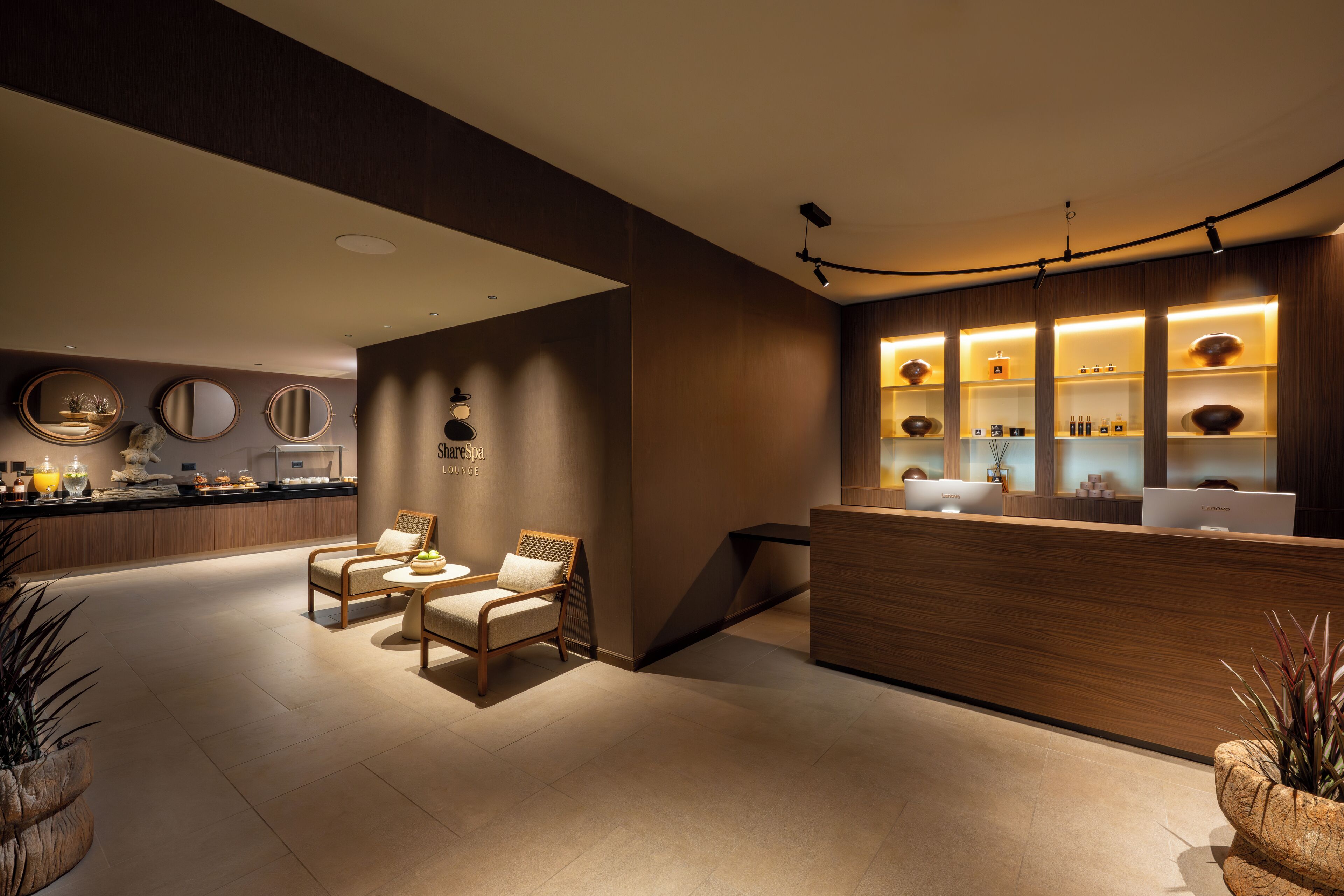 Un área de recepción moderna con mostrador de madera, zona de estar con sillas y una barra con diversos artículos.