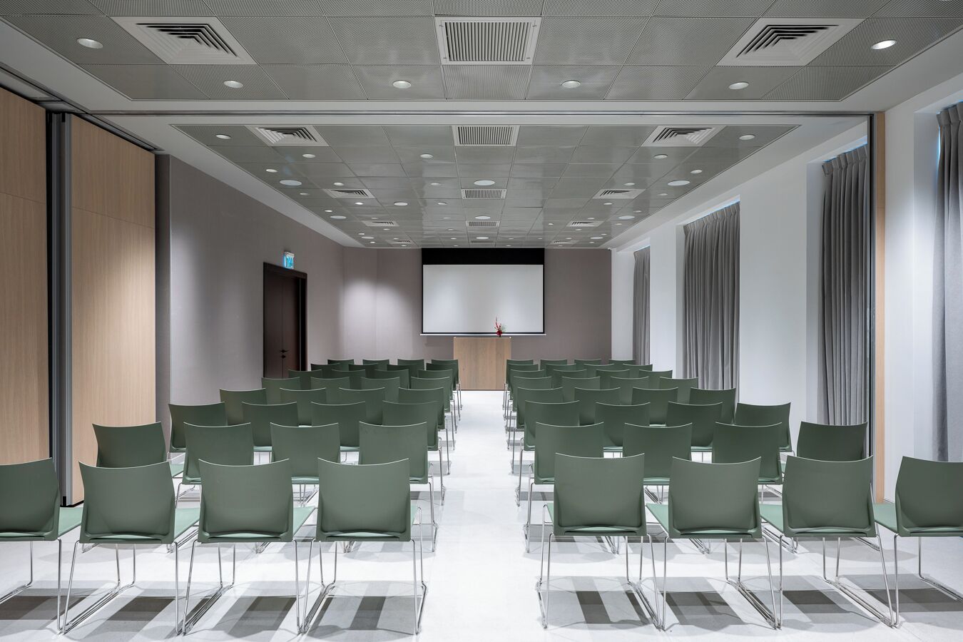 A conference room with rows of green chairs, a large screen, and a podium.