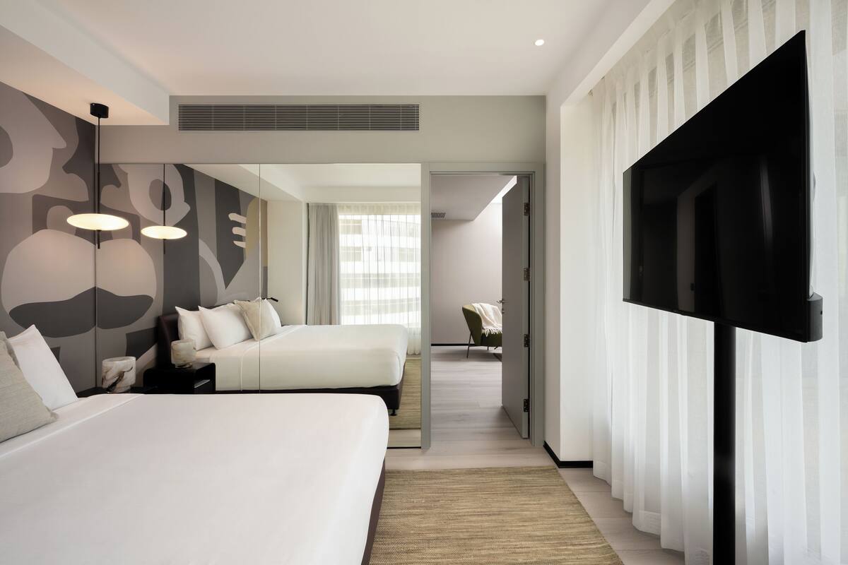 Une chambre d’hôtel moderne avec deux lits, une grande télévision et vue sur le couloir.
