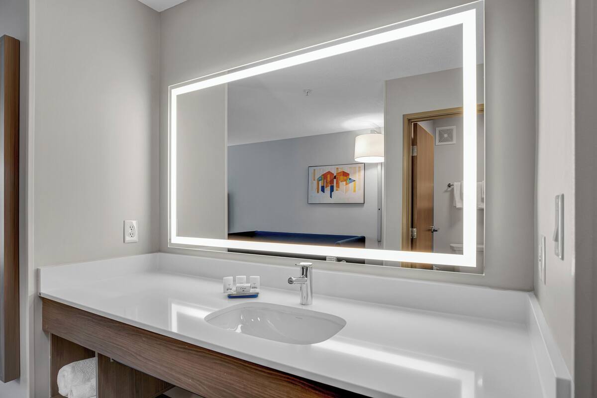 A modern bathroom with a white sink, a large mirror, and a wooden vanity.