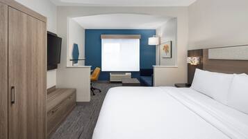 A hotel room with a large bed, a desk with a chair, a flat-screen TV, and a window with curtains.