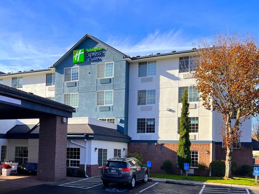 A Holiday Inn Express & Suites building with a clear sky, parking area, and a tree with autumn leaves.