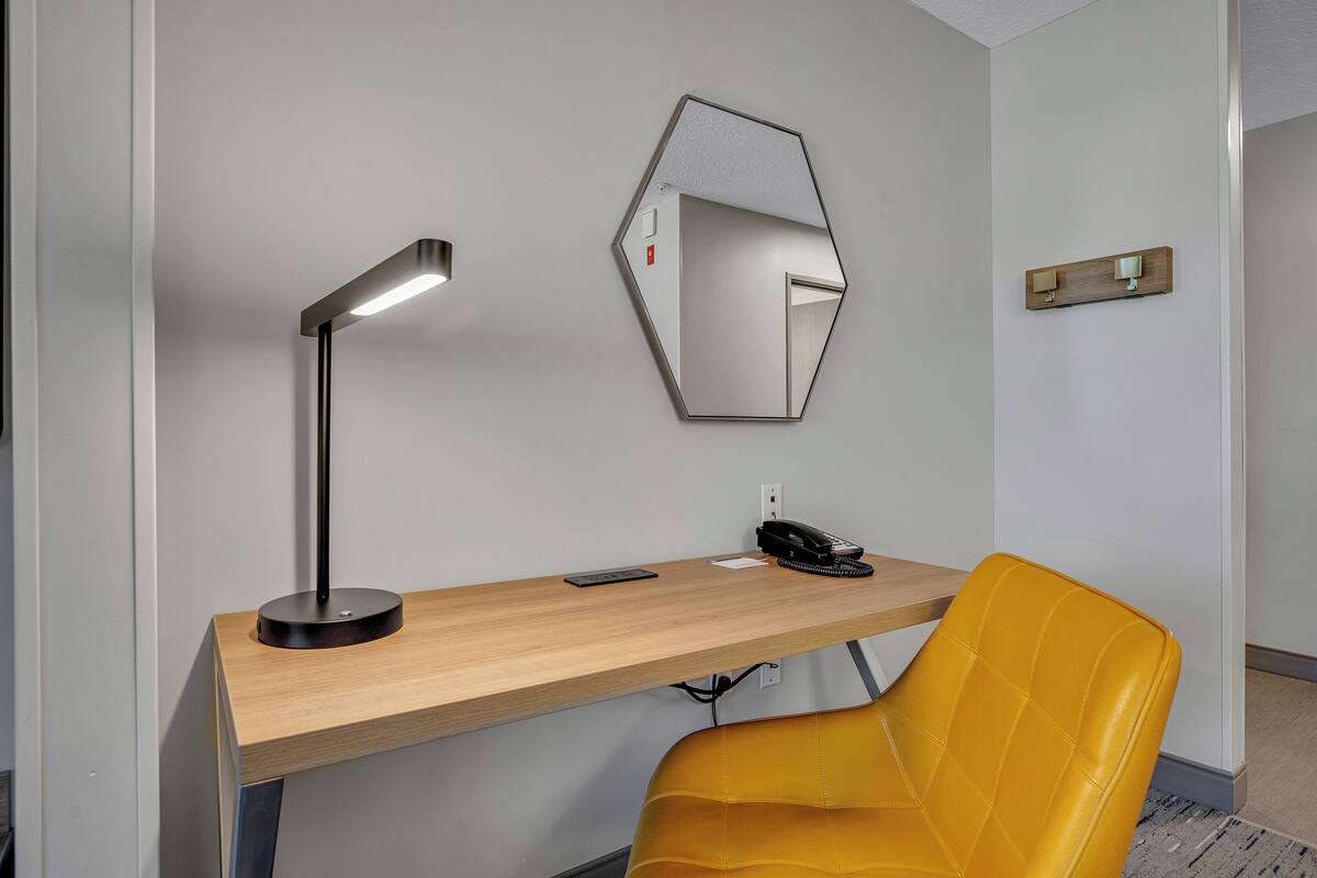 A modern office desk with a lamp, a phone, and a mirror.