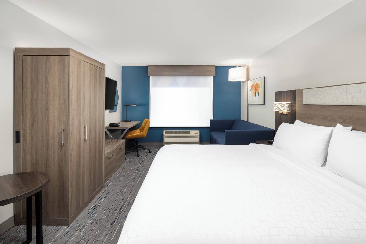 A hotel room with a large bed, a desk with a chair, a wardrobe, and a television on the wall.