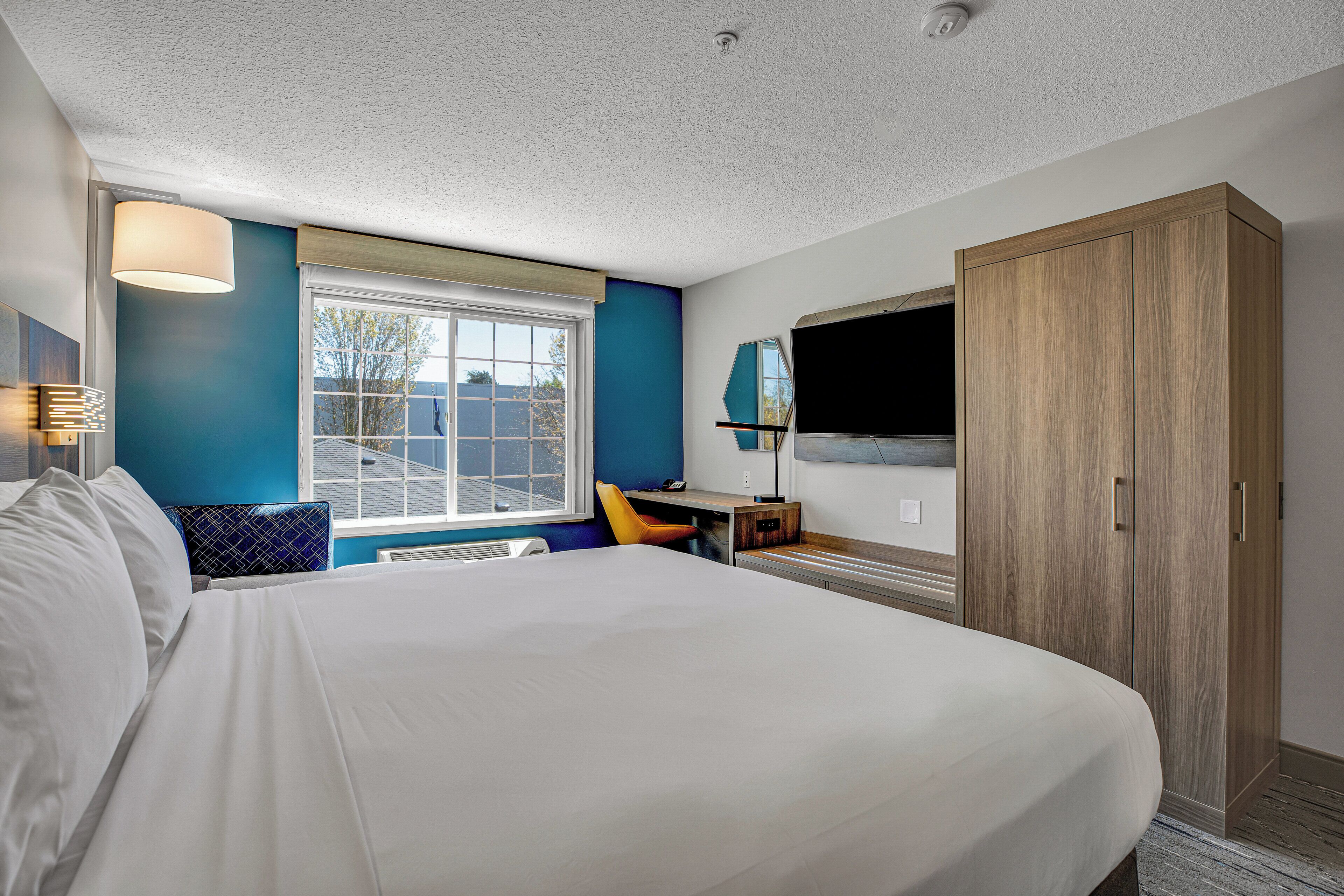 A hotel room with a large bed, a desk, a chair, a wardrobe, and a TV.