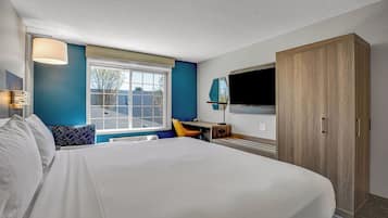 A hotel room with a large bed, a desk, a chair, a wardrobe, and a TV.