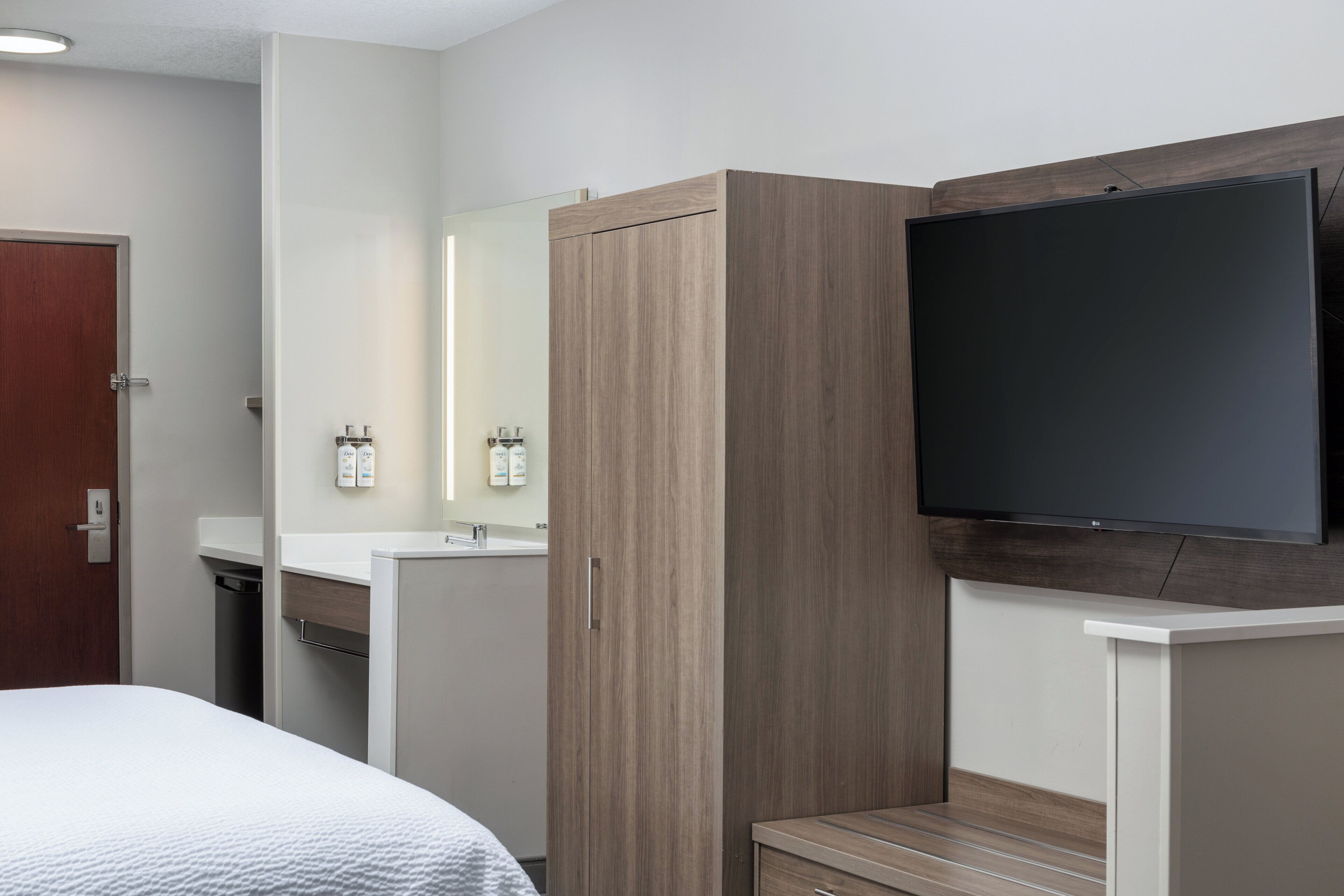 A hotel room with a bed, a wardrobe, a mirror, a television, and a small bathroom area.