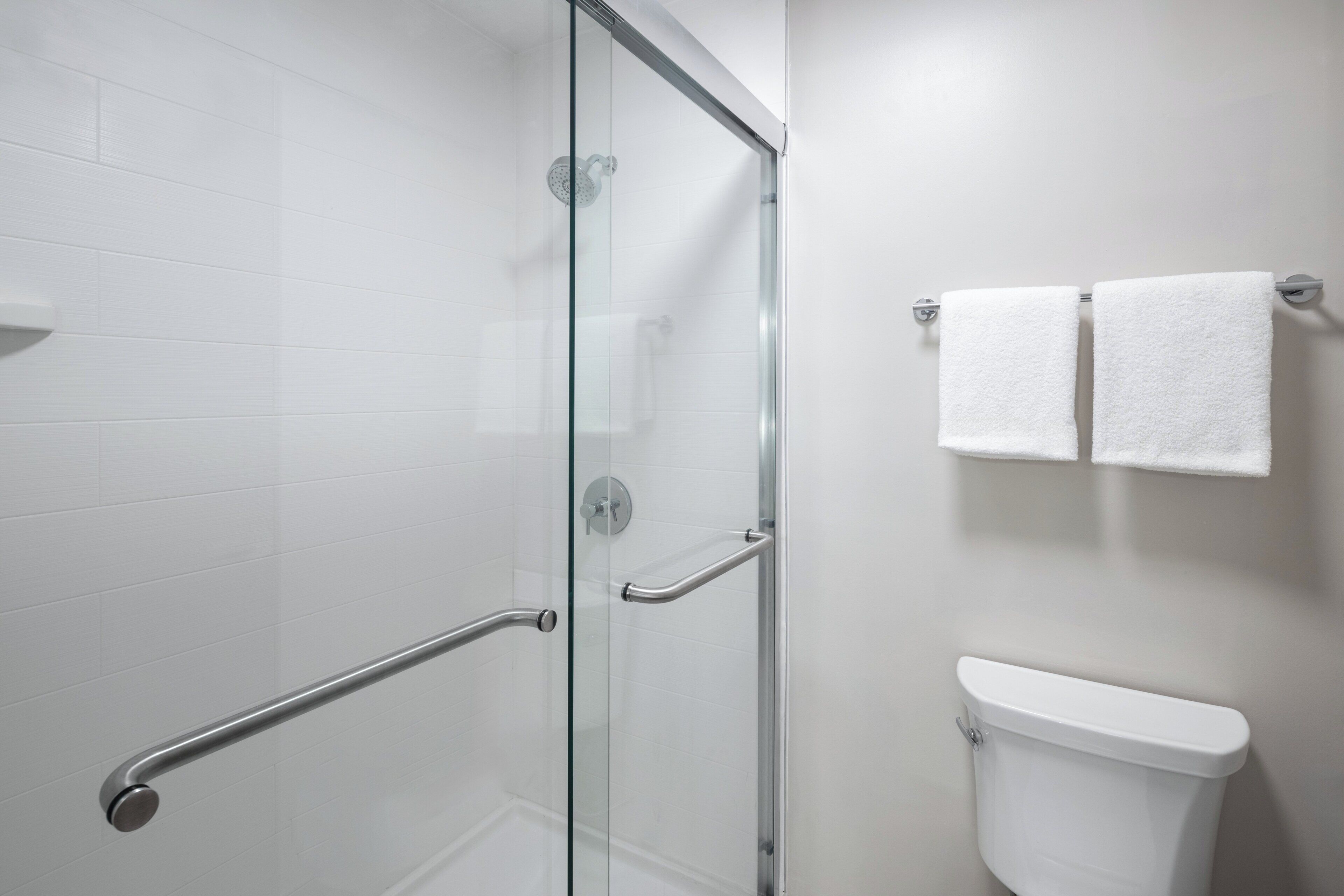 A bathroom with a glass shower enclosure, a white toilet, and two white towels hanging on a rack.