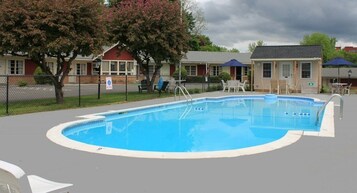 Una piscina rectangular con revestimiento azul, rodeada por una terraza gris. Se observan sillones de descanso y sombrillas al fondo.