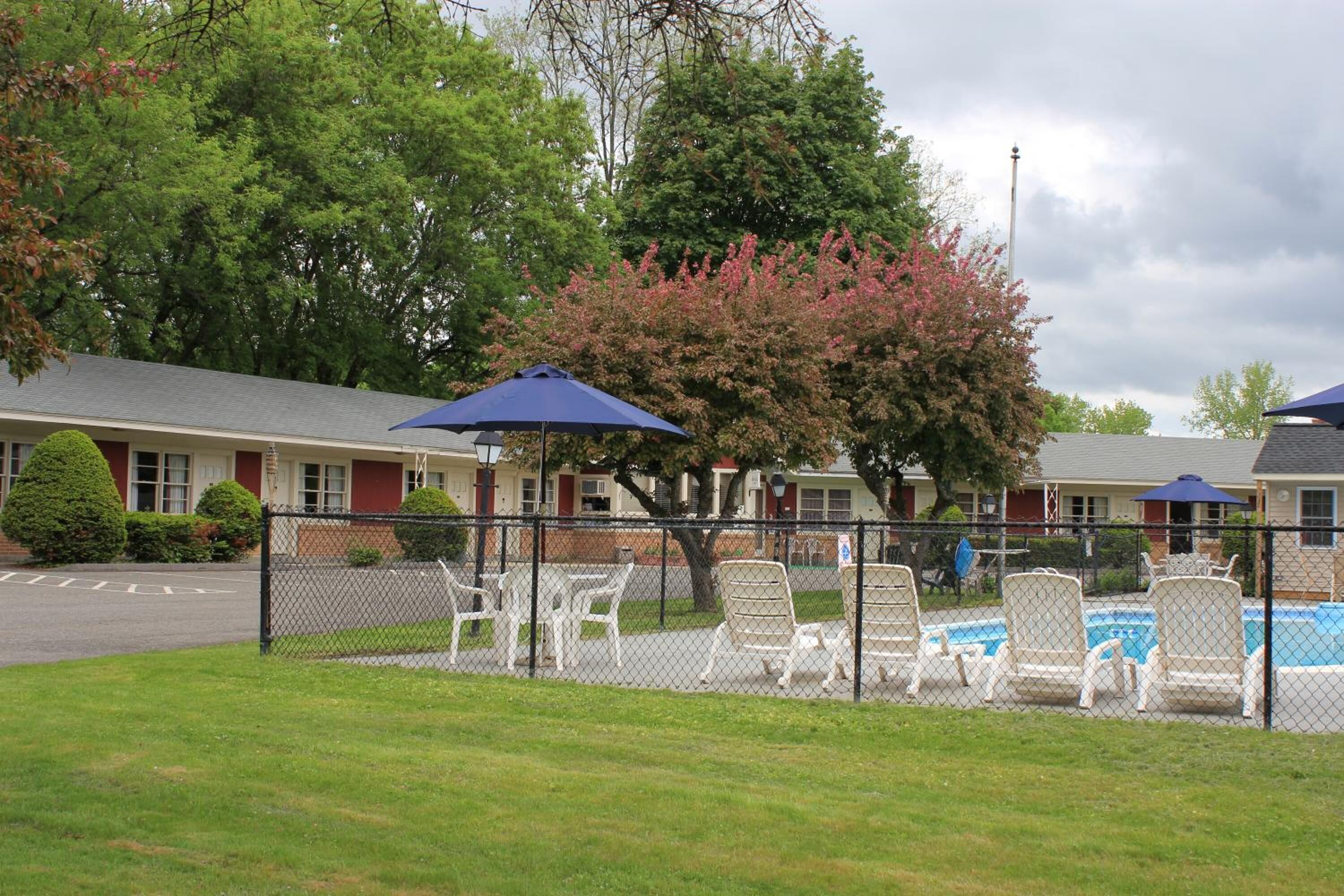 A fenced outdoor area with lounge chairs and umbrellas, a swimming pool, and a building with a red roof and white trim.