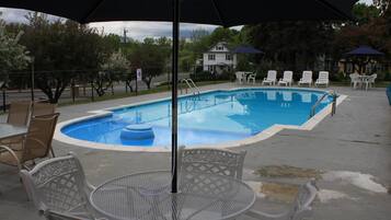 A swimming pool with lounge chairs and a table, surrounded by a fence and trees.