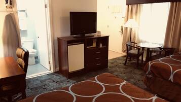 A hotel room with a bed, a desk, a chair, a television, a small cabinet, a bathroom visible through an open door, and a patterned rug.