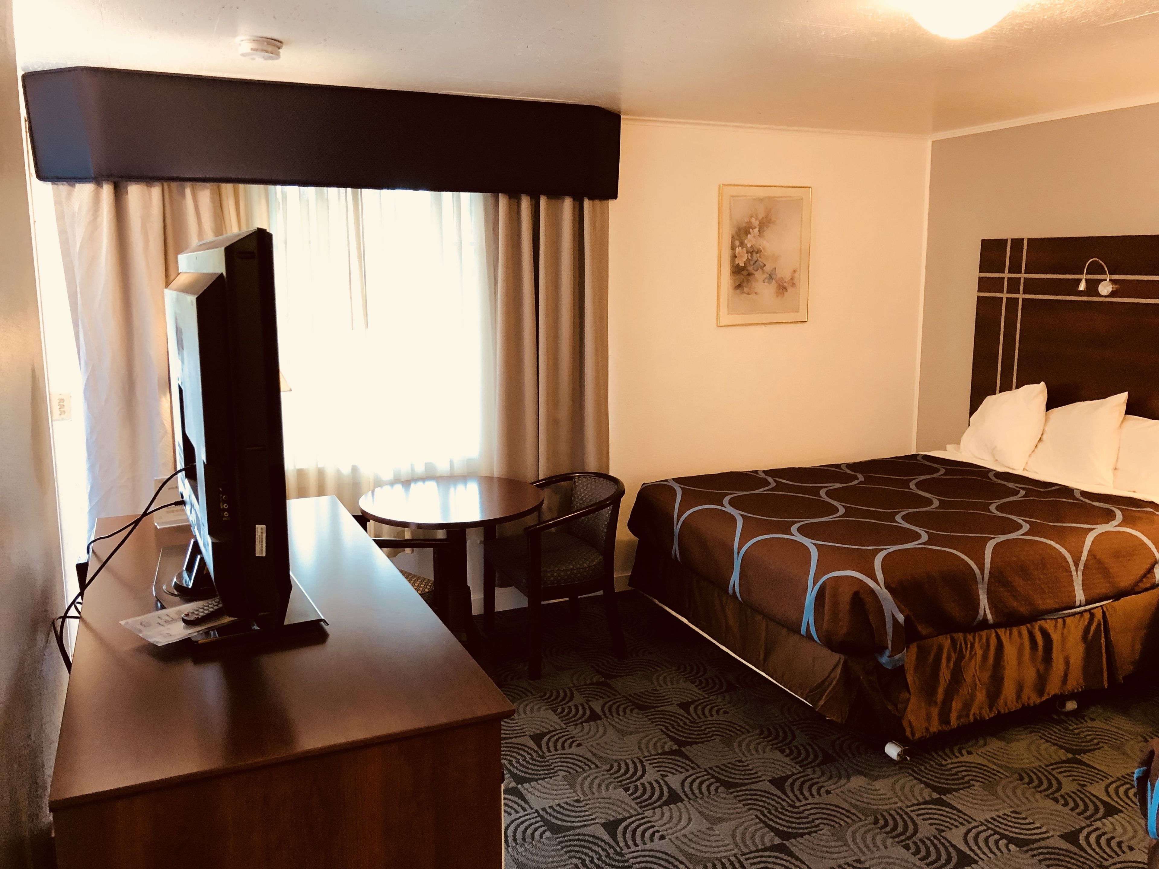 A hotel room with a bed, a desk with a television, a chair, and a small table.