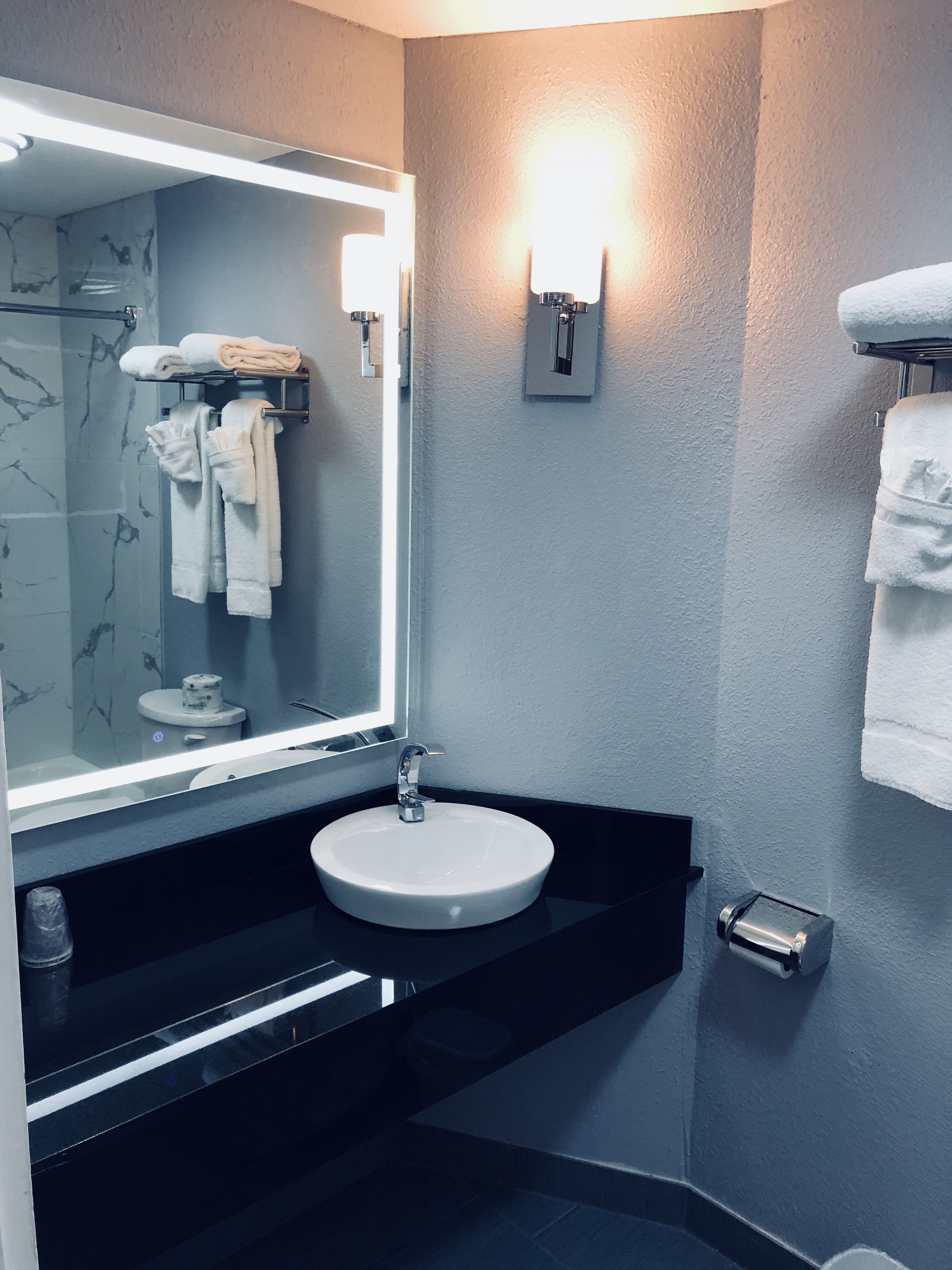 A modern bathroom with a large mirror, a round sink, and a towel rack.
