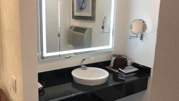 Ein Badezimmer mit Waschbecken, Spiegel mit Beleuchtung, Heizung und Mülleimer.
