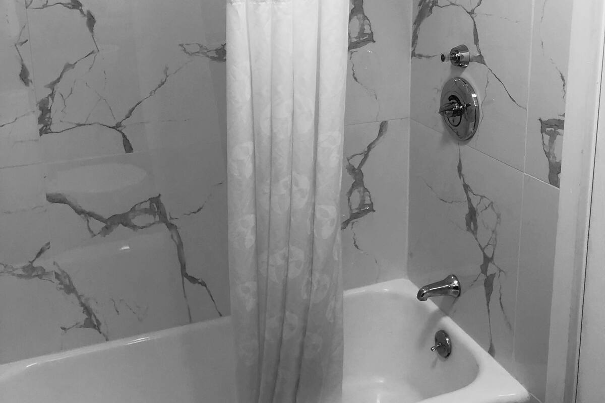 A bathroom with a marble-patterned wall, a shower curtain, a bathtub, and a handheld showerhead.