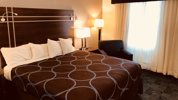 Quarto de hotel com uma cama grande, duas luminárias de cabeceira, uma cadeira e uma janela com cortinas.