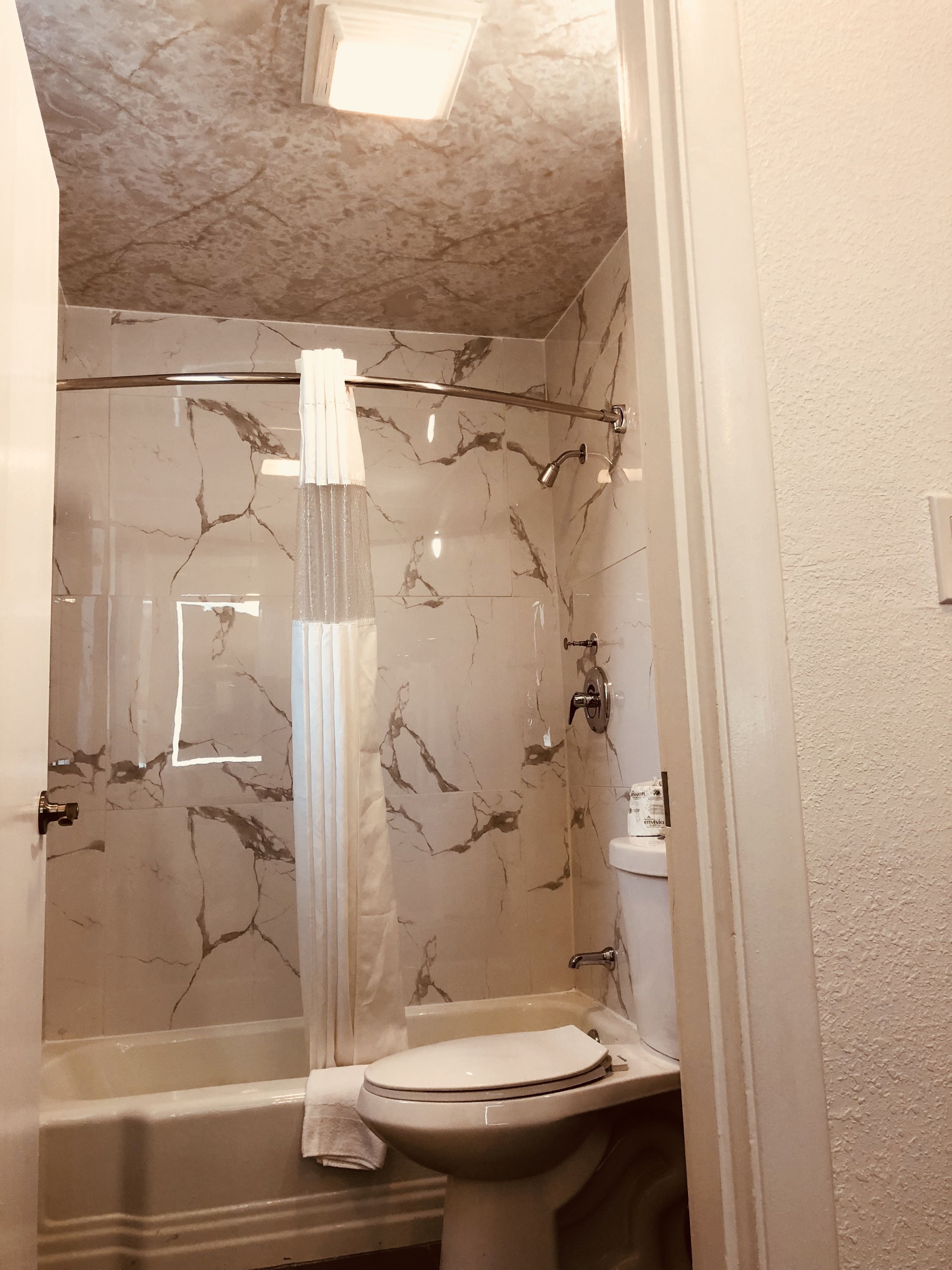 A bathroom with a marble shower wall, a glass shower enclosure, a white toilet, and a bathtub.