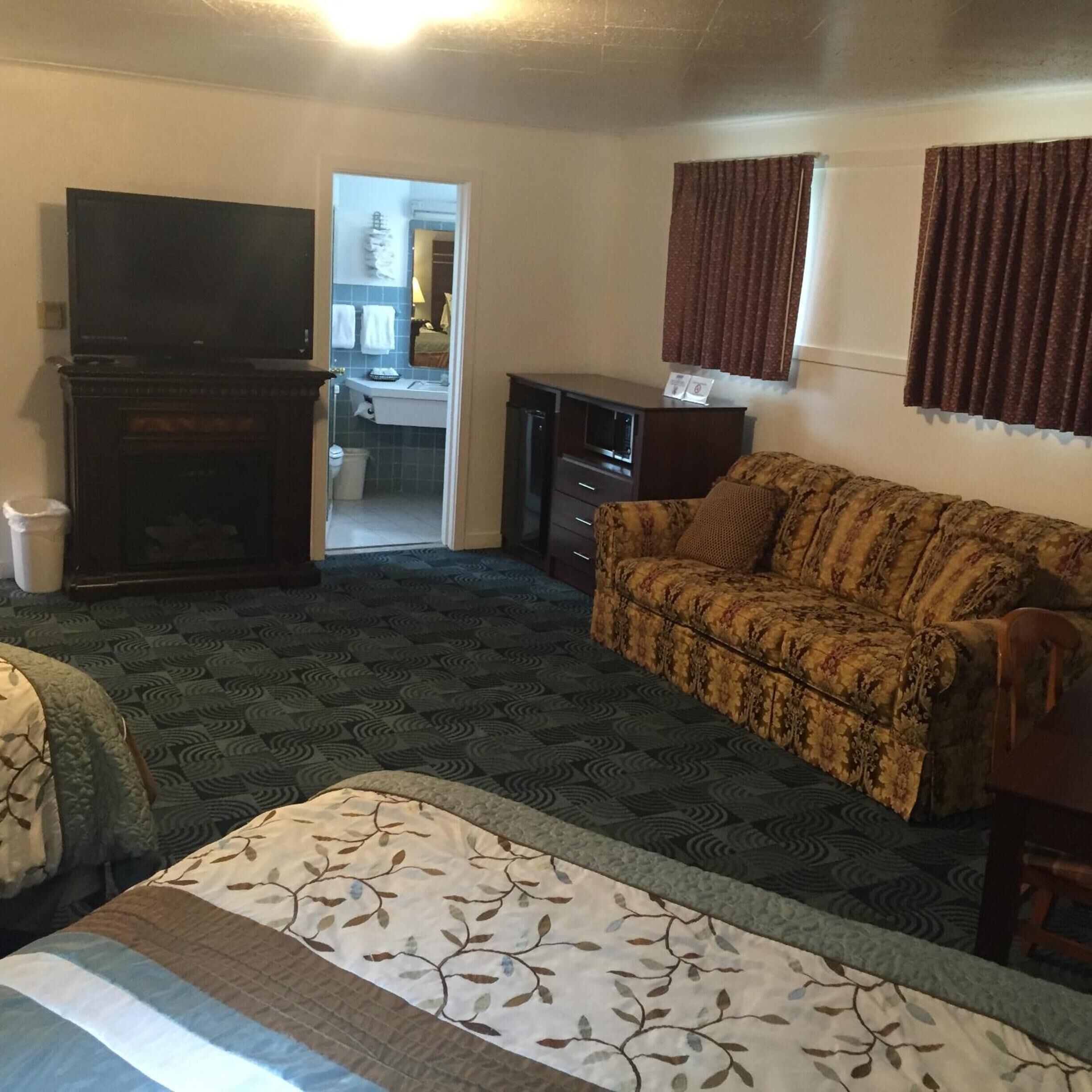 A hotel room with a bed, a sofa, a television, a desk, and a bathroom visible through an open door.
