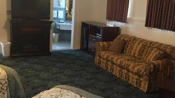 A hotel room with a bed, a sofa, a television, a desk, and a bathroom visible through an open door.