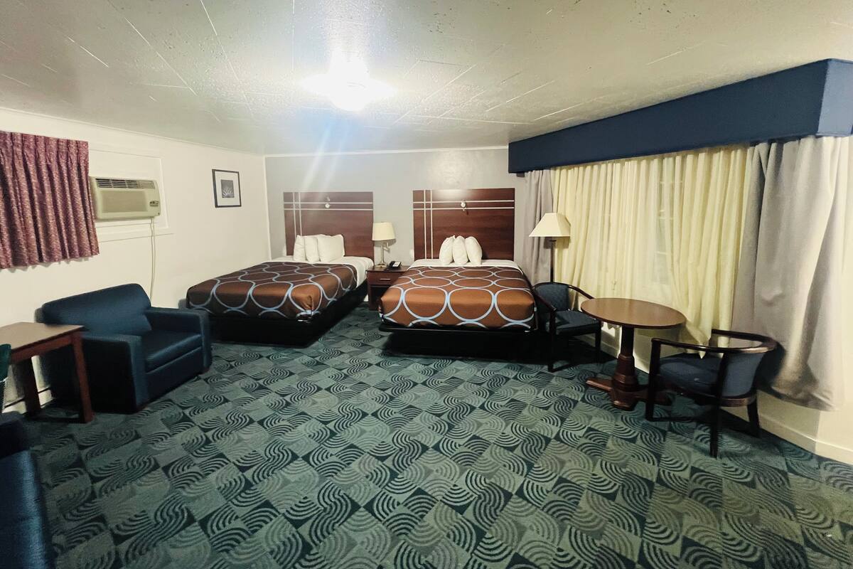 A hotel room with two beds, a desk, a chair, a small table, and a window with curtains.