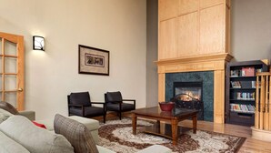 A living room with a fireplace, two armchairs, a sofa, a coffee table, and a bookshelf. - Country Inn & Suites by Radisson, Milwaukee Airport, WI (Milwaukee)