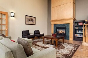Una sala de estar con chimenea, dos sillones, un sofá, una mesa de centro y una estantería.