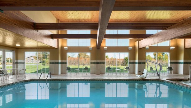 A large indoor swimming pool with clear blue water, wooden beams on the ceiling, and multiple windows offering views of the surrounding area. - Country Inn & Suites by Radisson, Milwaukee Airport, WI (Milwaukee)