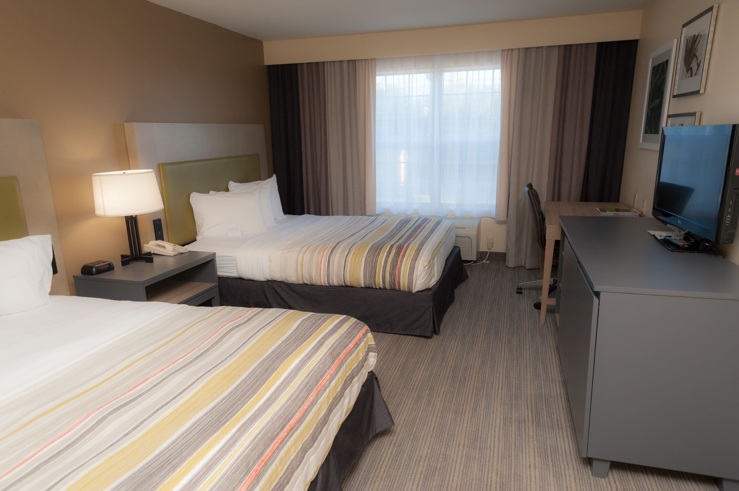 A hotel room with two beds, a desk, a television, and a window with curtains.