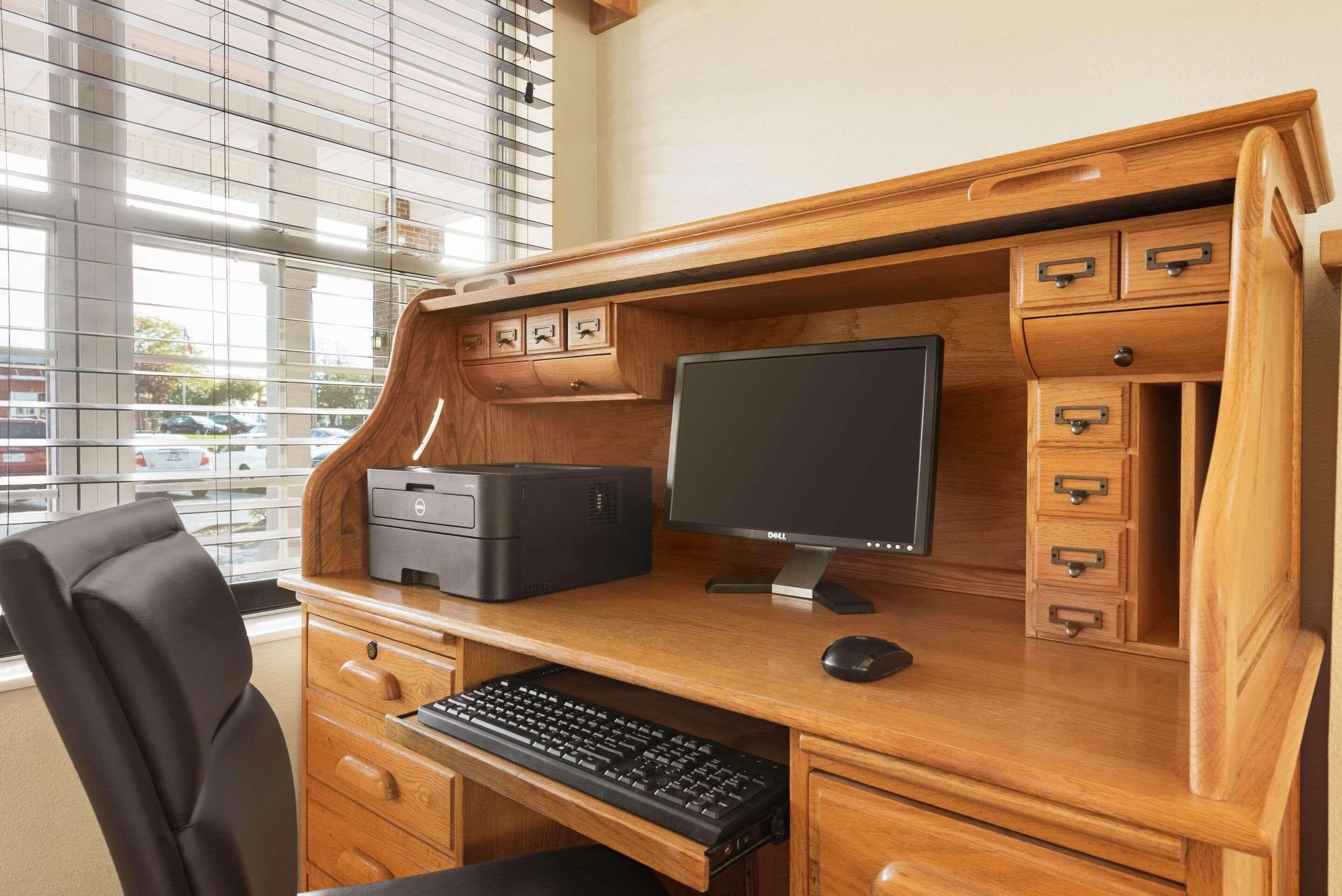 A wooden desk with a Dell monitor, keyboard, and printer. There are drawers and a small cabinet with handles.