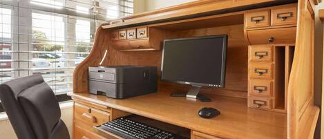 Een houten bureau met een Dell monitor, toetsenbord en printer. Er zijn lades en een klein kastje met handgrepen.