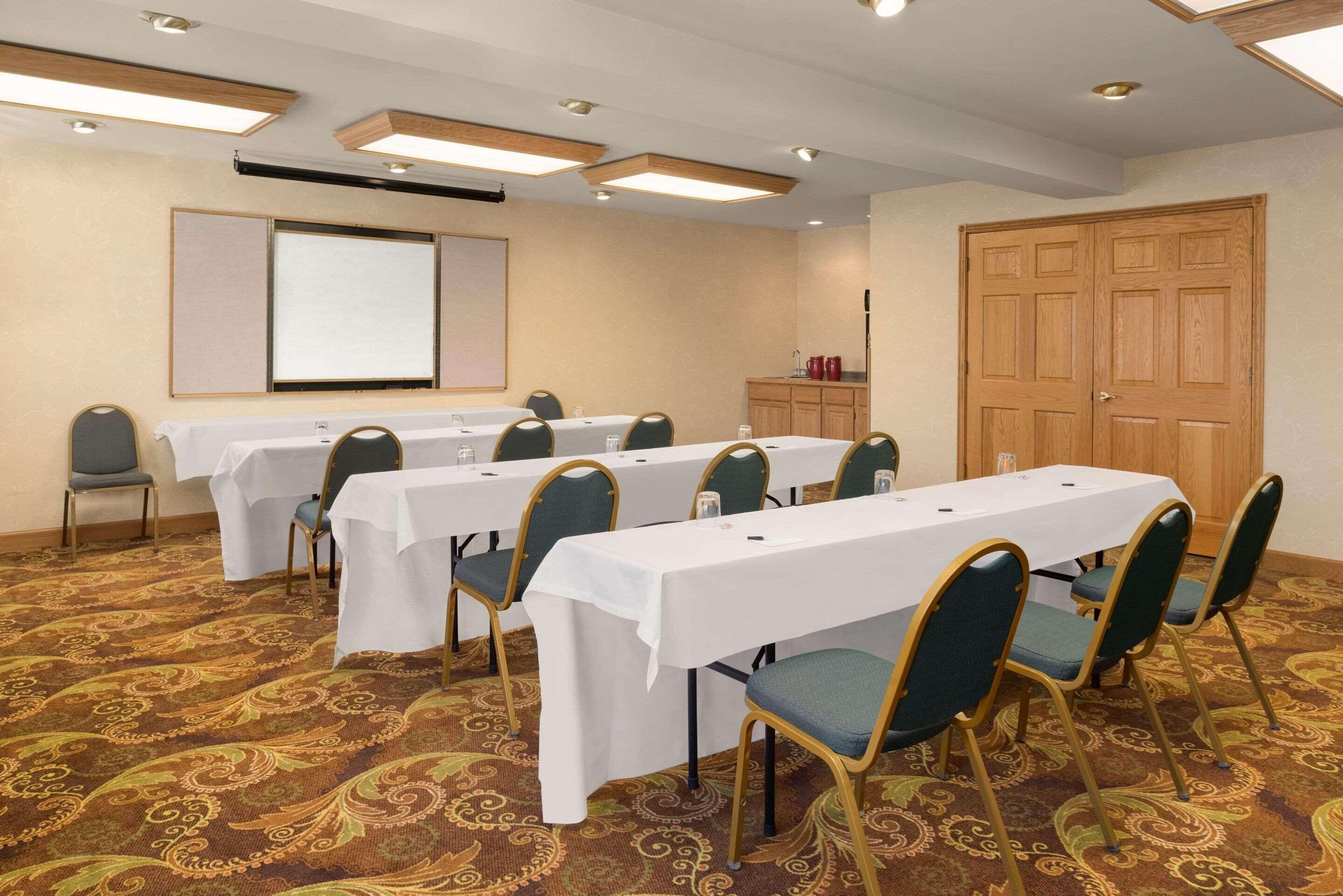 A conference room with multiple tables and chairs, a projector screen, and a wooden door.
