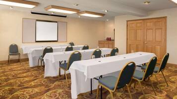 A conference room with multiple tables and chairs, a projector screen, and a wooden door.
