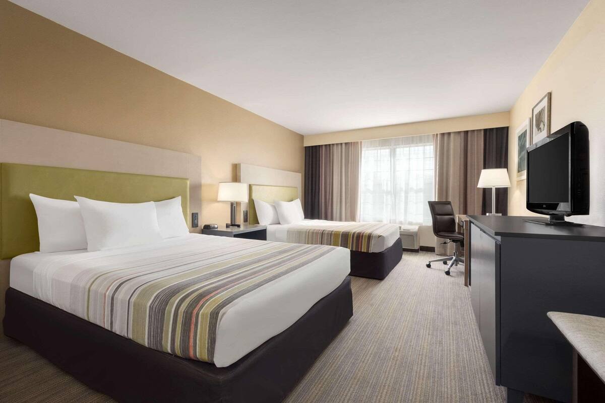 A hotel room with two beds, a desk, a chair, a TV, and a window with curtains.