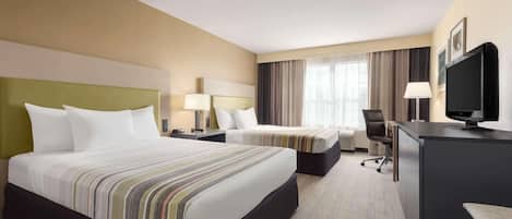A hotel room with two beds, a desk, a chair, a TV, and a window with curtains.