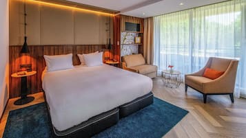 Ein modernes Hotelzimmer mit einem großen Bett, einer Sitzecke mit Sessel und kleinem Tisch sowie einem großen Fenster mit Vorhängen.