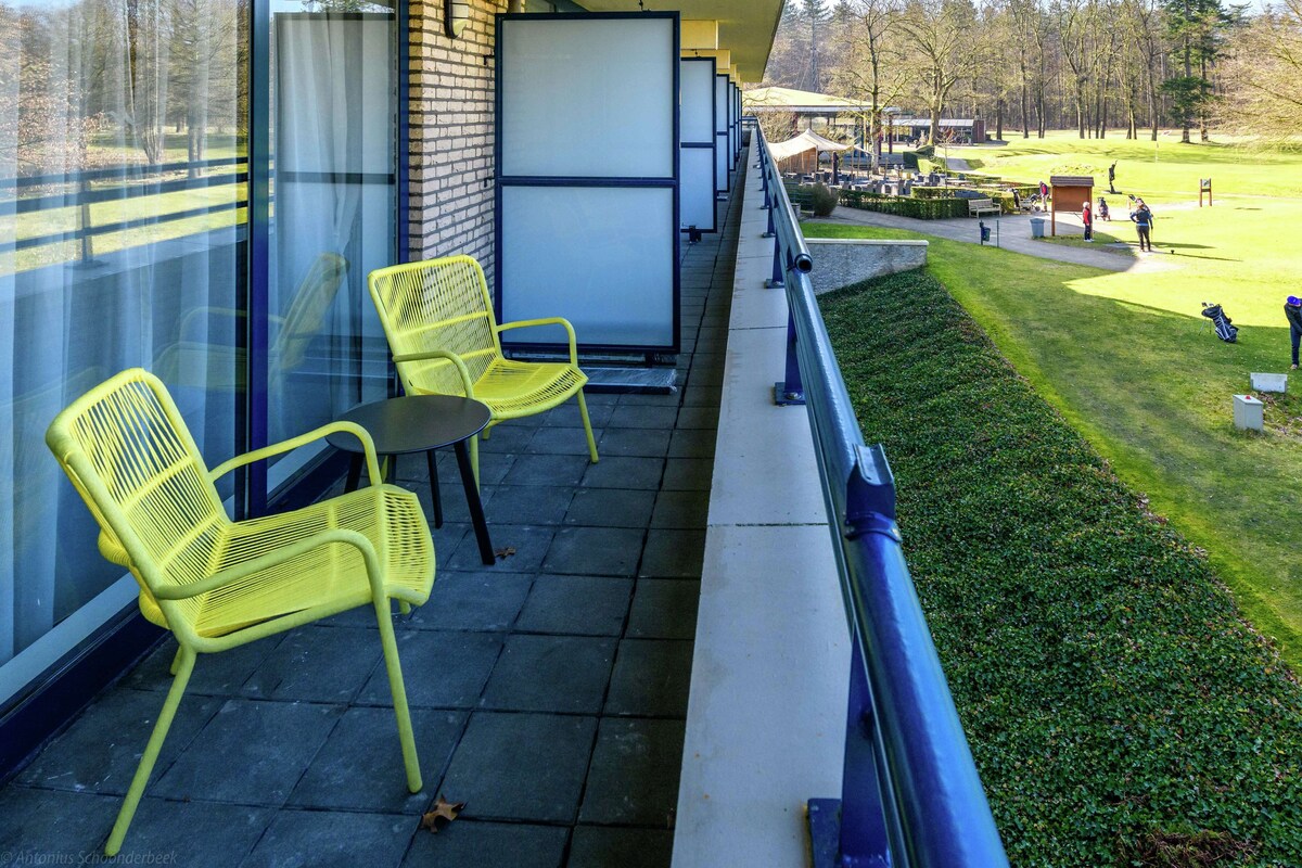 A balcony with yellow chairs and a table, overlooking a golf course.