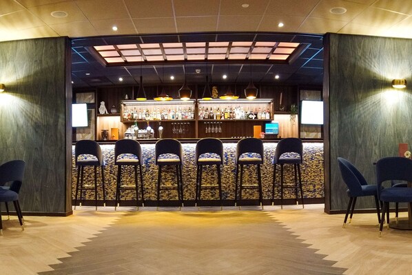 A bar area with a counter, multiple stools, and a variety of bottles. - DoubleTree by Hilton Royal Parc Soestduinen (Soest)