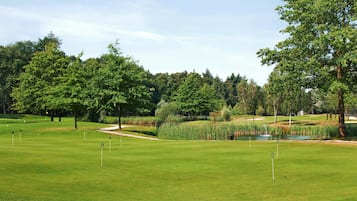 A well-maintained golf course with clear fairways, sand traps, and a pond.